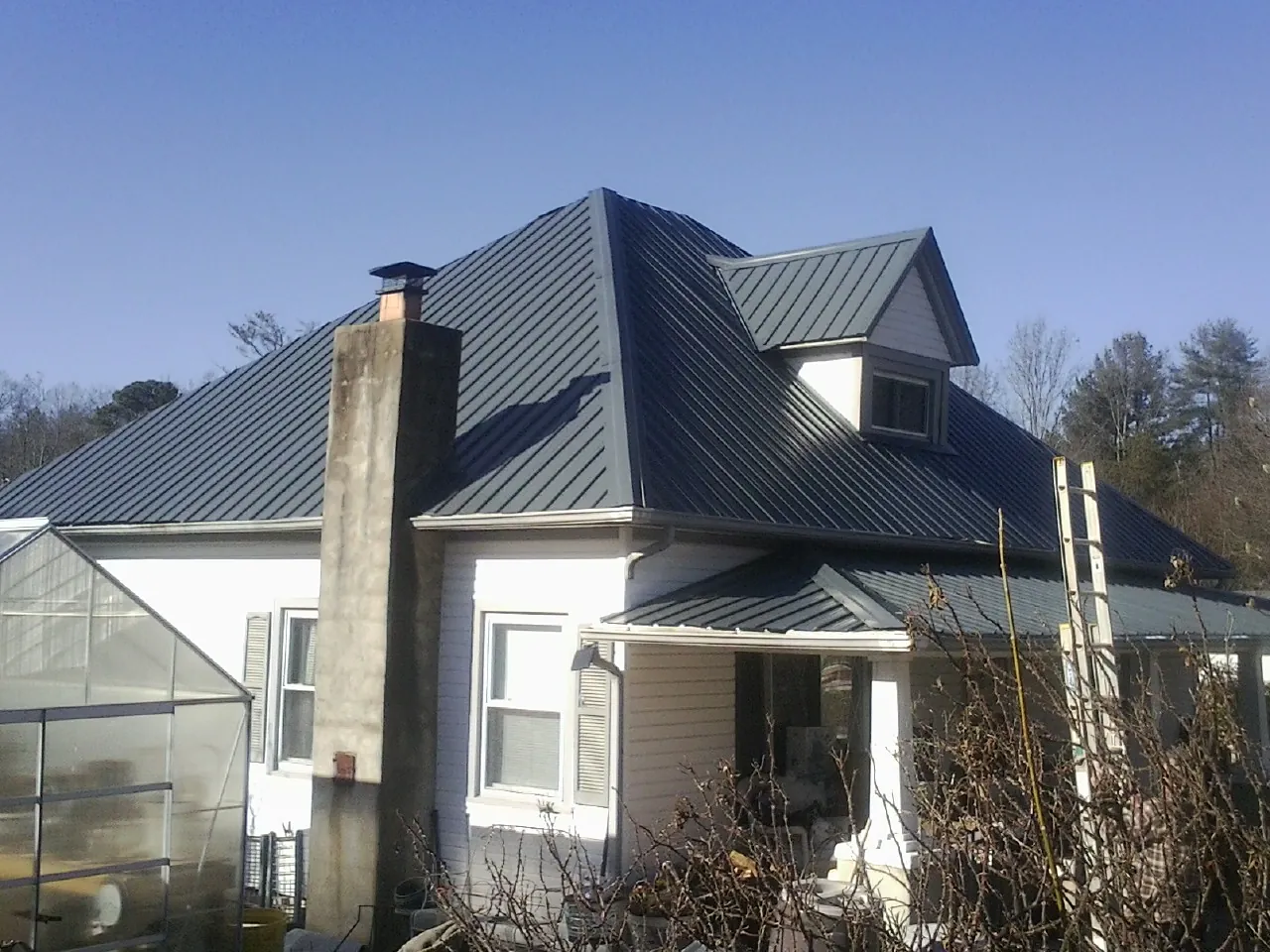 Dark blue standing seam metal roof on a white farmhouse with dormer — Slate & Tile Roof Repair by Roofing Brothers in Ulen