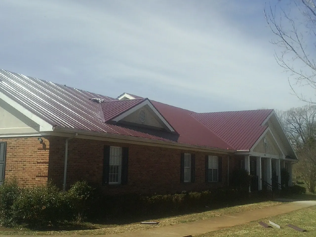 Red metal roof with gabled entries on a long brick building, from a Hail Damage Roof Repair job in Ulen