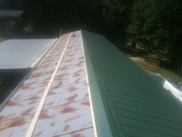 Old rusted panels beside newly installed green metal roofing — Wind Damage Roof Repair by Roofing Brothers in Ulen