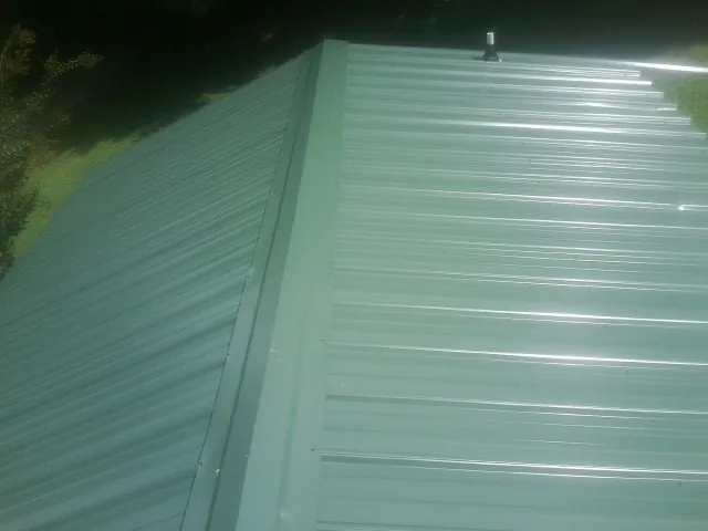 New green metal panels meeting at the ridge of a roof — Flat Roof Repair work by our crew in Ulen