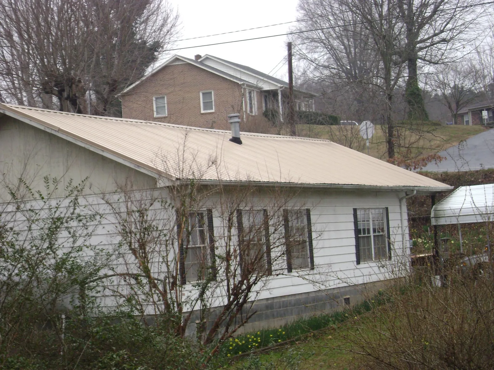 Tan metal roof on a white sided house set into a hillside — Commercial Roofing by Roofing Brothers in Ulen