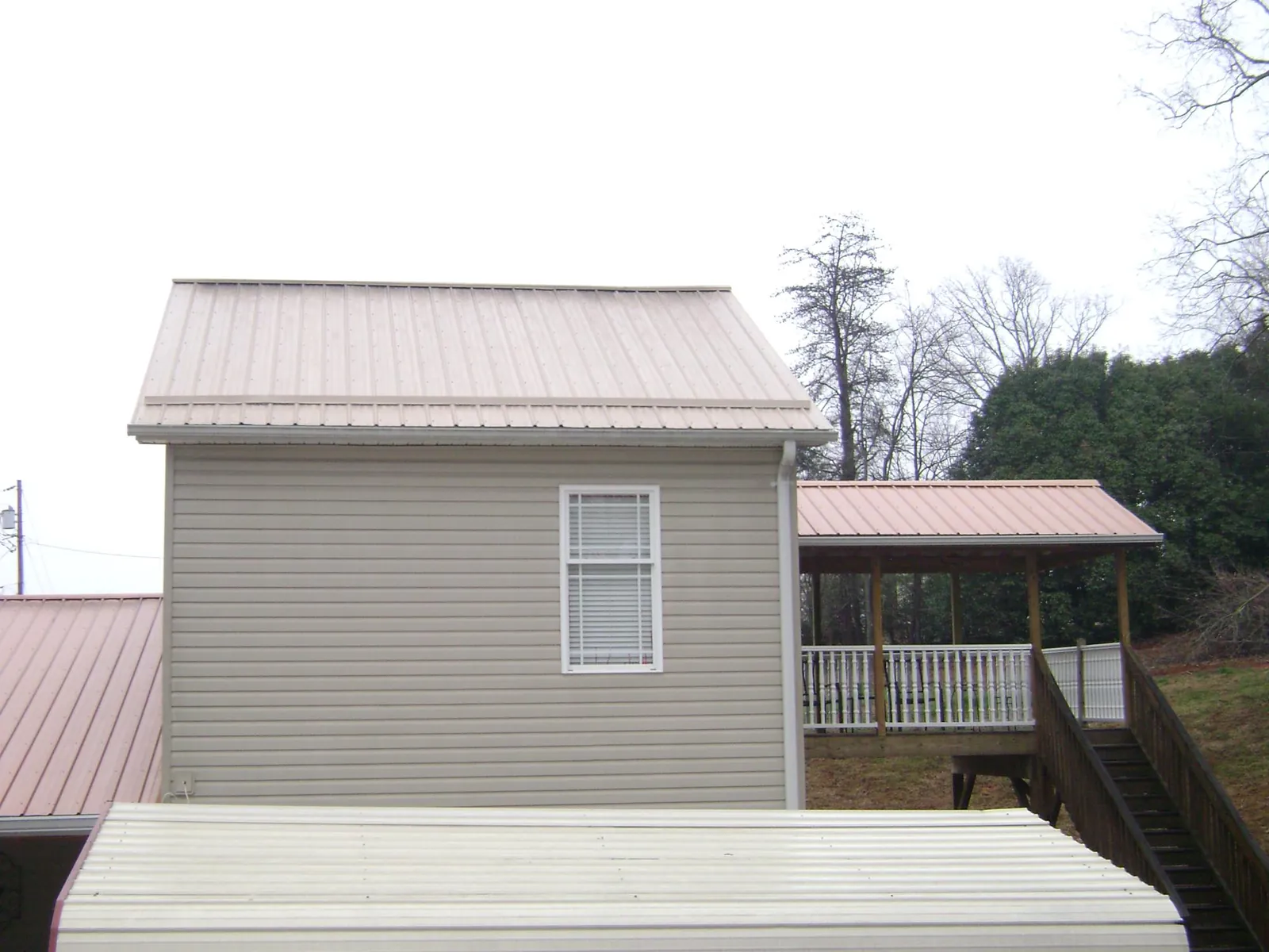 Tan metal roofs on a two story addition and attached porch, from a Roof Replacement job in Ulen